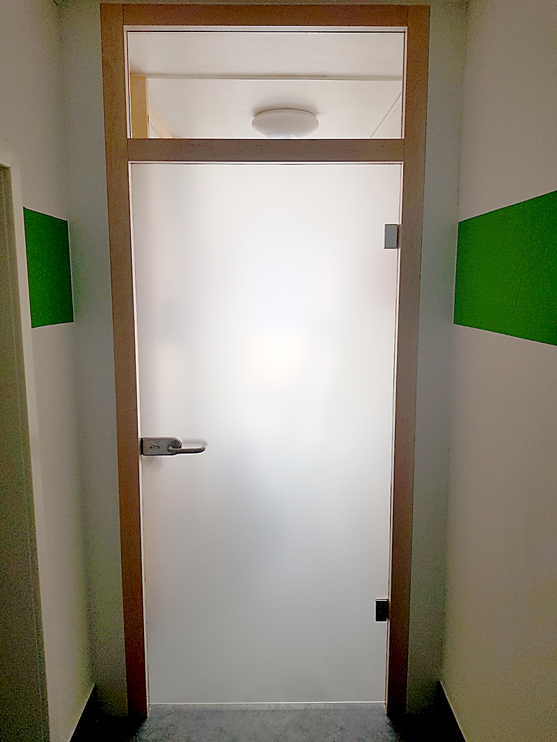 Windfangelement in Ahorn lackiert mit weissen Rahmenverbreiterungen. Ganzglastür Satinato. Oberlicht in Klarglas. Beschlag verschließbar.